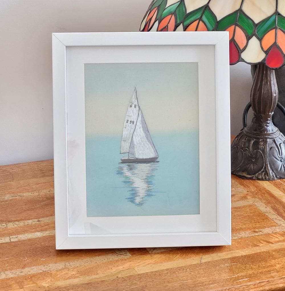 Original embroidery of a sailing boat on calm waters showing the reflection on the sea. 23 x 28 cm in total size including the frame.