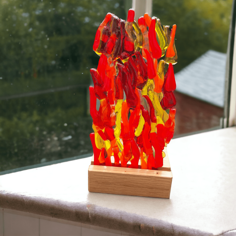 A photo of a glass candle holder on a wooden stand. The clear glass holder features a colourful fused glass design with red and orange glass on the front. It rests on a wooden base