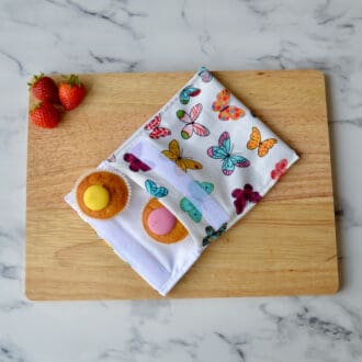 A snack bag with a butterfly pattern is placed on a wooden board alongside cupcakes and strawberries.