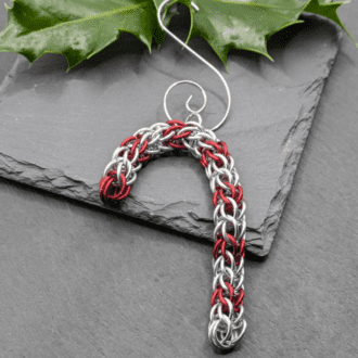 A chainmaille Christmas decoration in the shape of a candy cane made from red and silver rings.