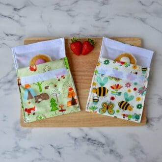 One forest animals and one busy bugs snack bag on a wooden board with strawberries and cupcakes.