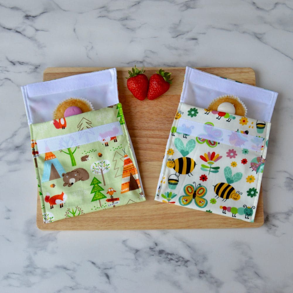 One forest animals and one busy bugs snack bag on a wooden board with strawberries and cupcakes.