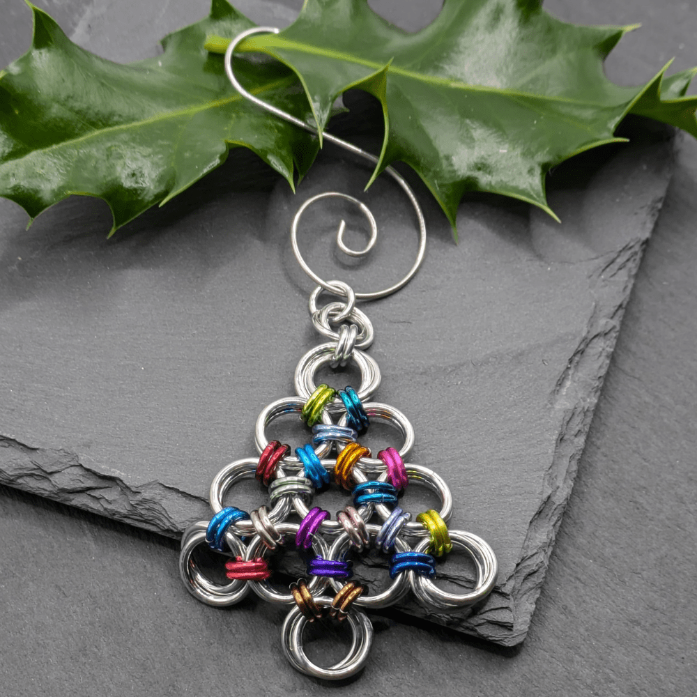 A chainmaille Christmas decoration in the shape of a Christmas tree made from silver and lots of different coloured aluminium rings.