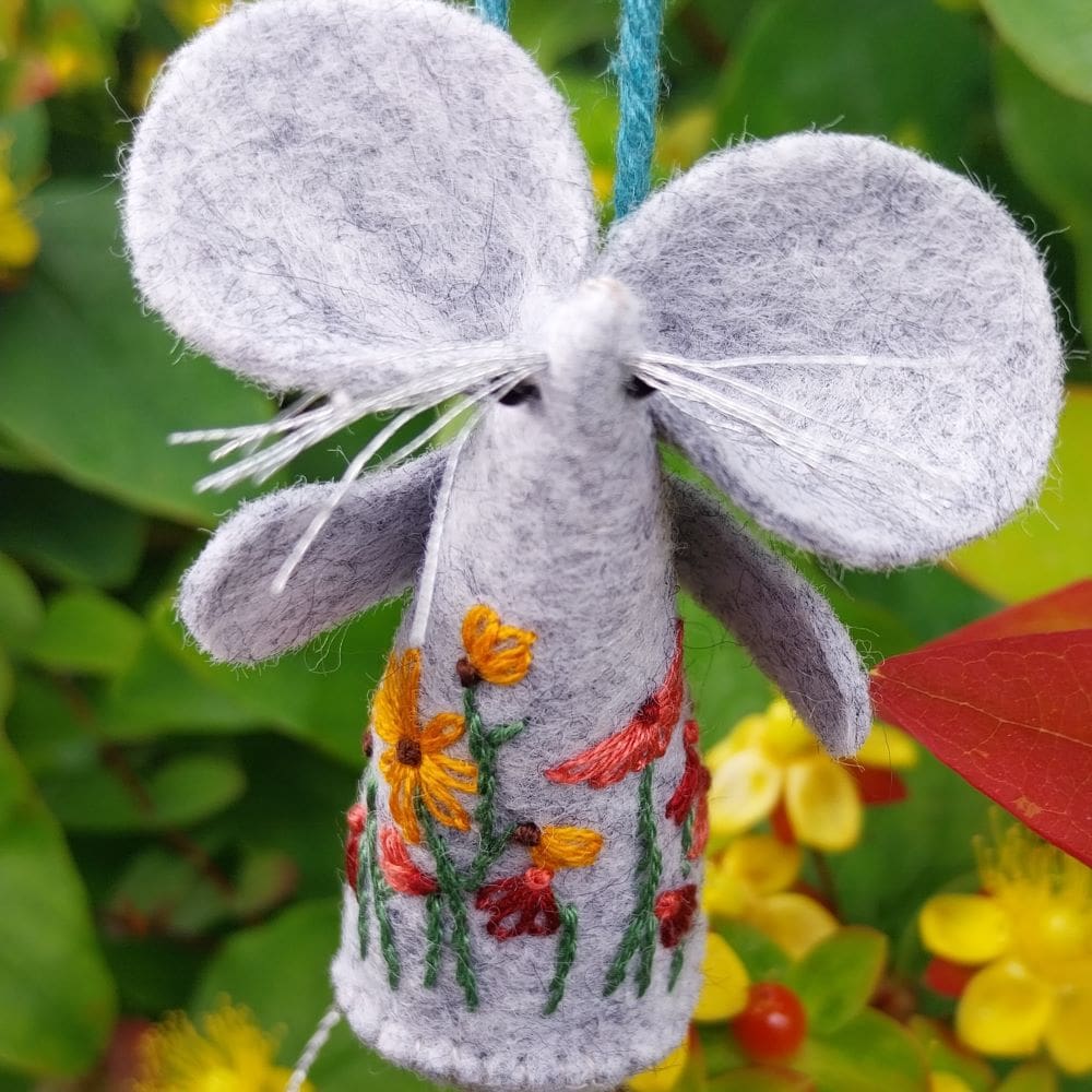 A hand embroidered and stitched felt mouse with a design of daisies.