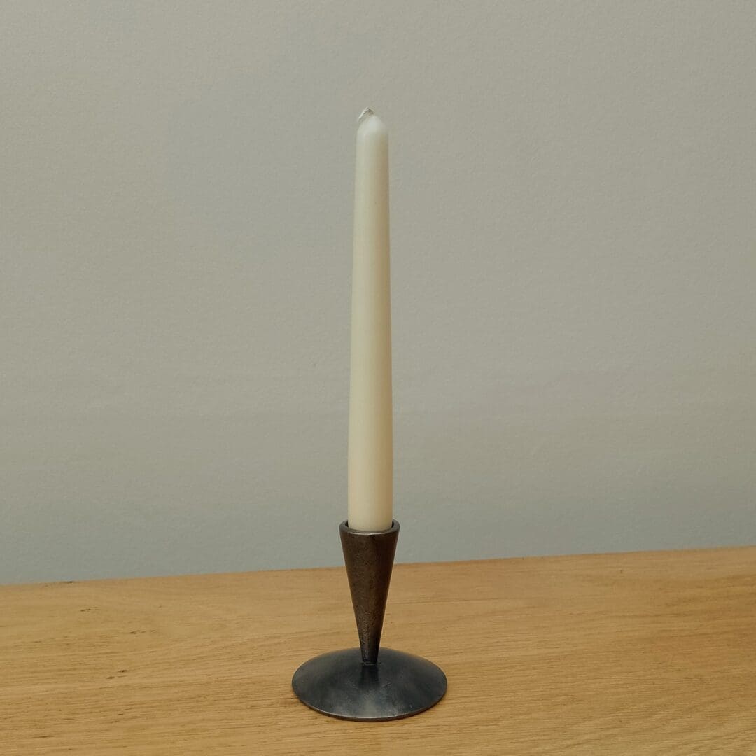 This is a hand forged candle holder, I make them in my Warwickshire workshop. They are approximately 9cm high, 9cm wide and 9cm deep but as they are hand made they may vary slightly. I use mild steel to create them in the forge, once the hot metal has been worked I remove any scale with a wire brush and then coat the metal with beeswax to protect it and give it a beautiful sheen. They make ideal gifts for 6th and 11th wedding anniversaries. They suit both traditional and contemporary homes.