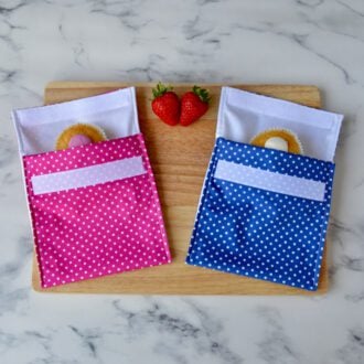 Pink and blue polka dot snack bags on a wooden board with cupcakes inside and fresh strawberries placed around them.