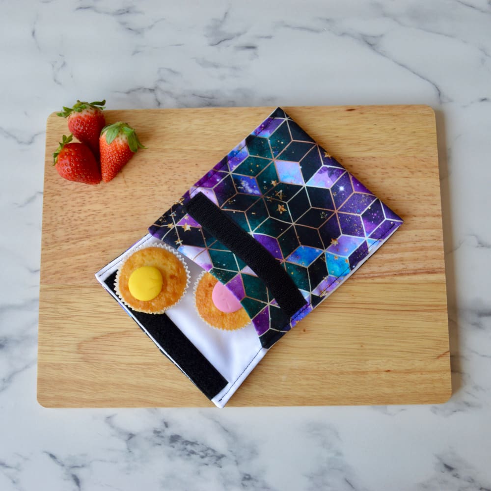 A purple geometric snack bag is displayed on a wooden board with cupcakes and strawberries. A purple geometric snack bag is displayed on a wooden board with cupcakes and strawberries. A purple geometric snack bag is displayed on a wooden board with cupcakes and strawberries.