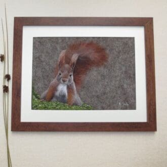 A handmade needle felted wool picture of a red squirrel sitting on green moss in a dark wood frame.