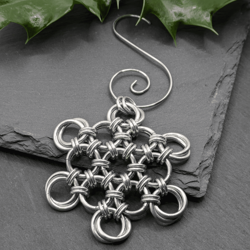 A chainmaille Christmas decoration in the shape of a snowflake made from silver aluminium rings.
