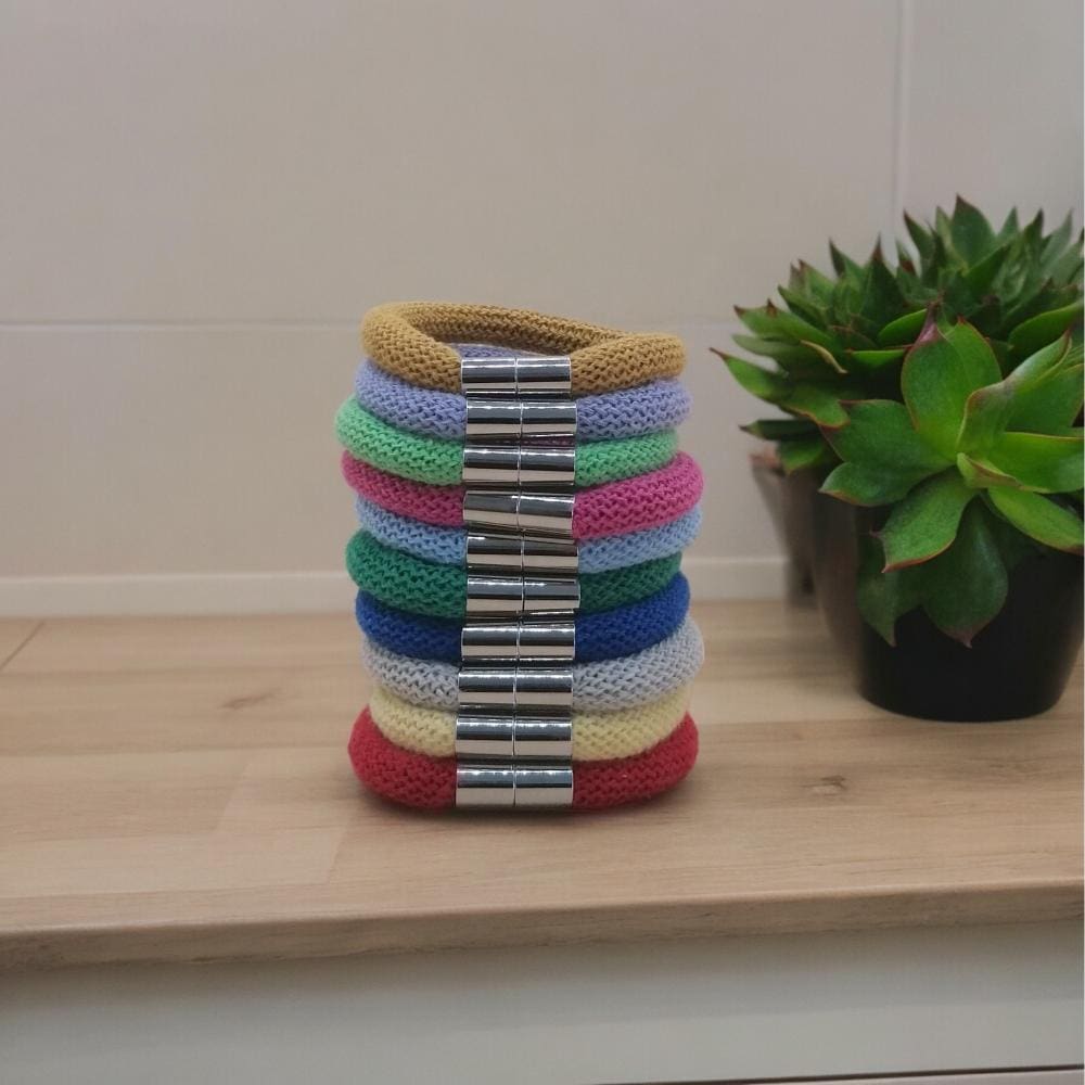 Stack of chunky stackable colourful bracelets shown on a wooden work top against a light background.