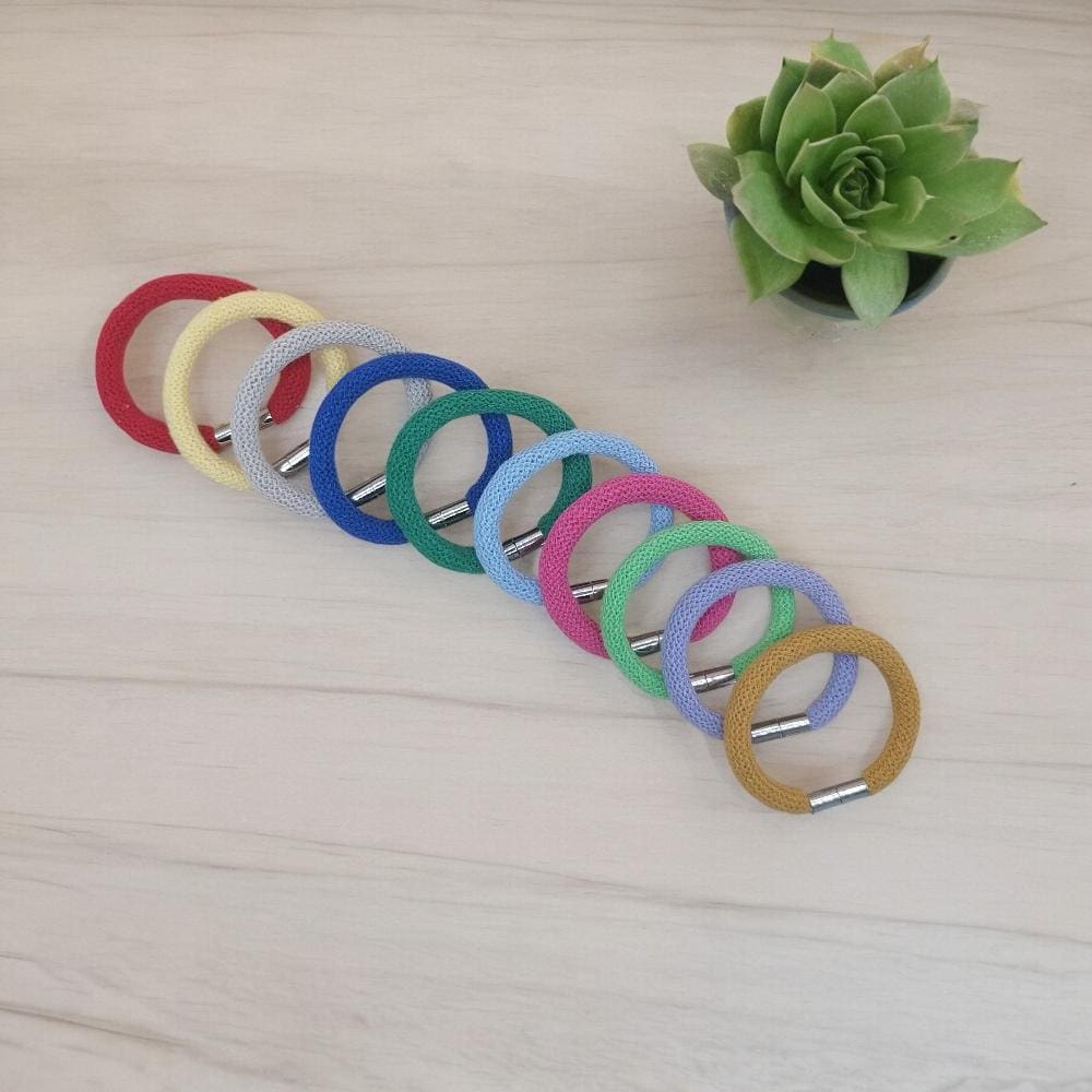 group of colourful chunky bracelets laid side by side viewed from above against a pail wood countertop surface.