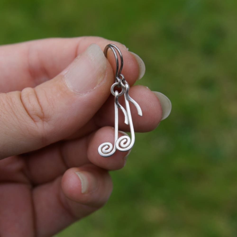 Hand holding sterling silver quaver note earrings by Oruki Design