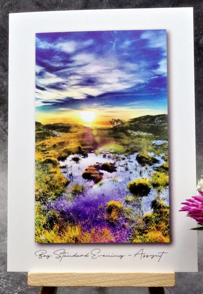 Larger image showing an A6 size greetings card, blank inside, on a small easel displaying a sunset evening view of a boggy place on a highland croft in Assynt!