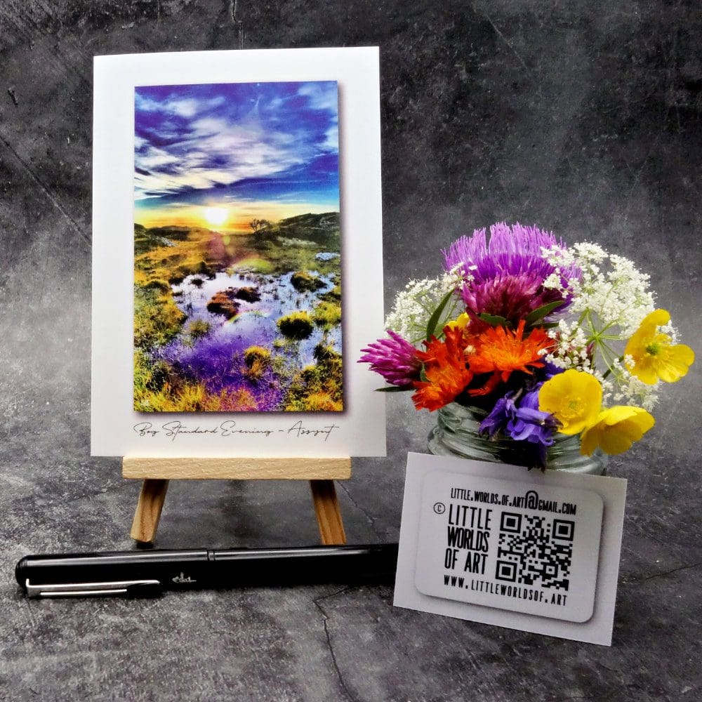 Image showing an A6 size greetings card, blank inside, on a small easel displaying a sunset evening view of a boggy place on a highland croft in Assynt!