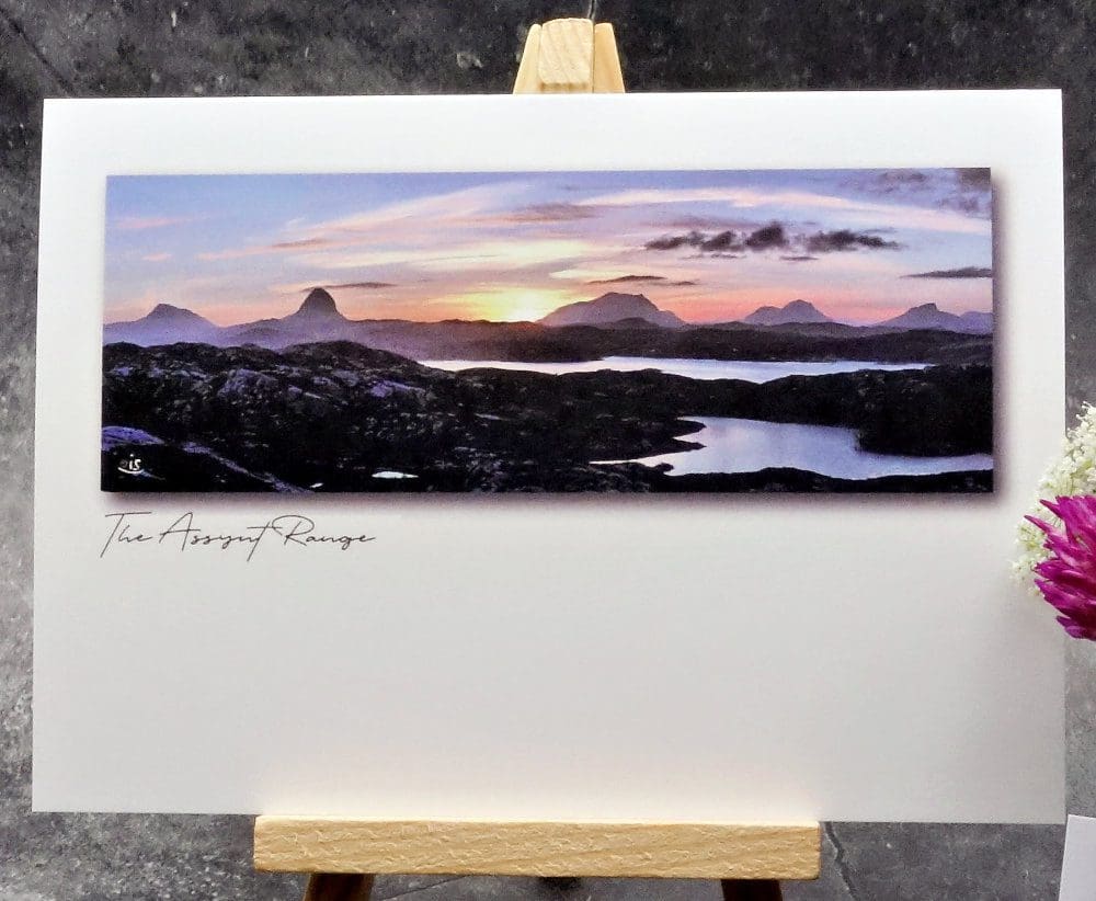 Larger image showing an A6 size greetings card, blank inside, on a small easel displaying a morning sunrise over the Assynt mountain range.