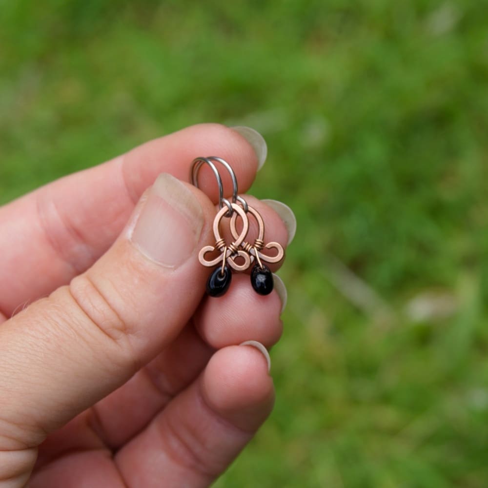 hand holding a pair of handmade copper earrings with black beads