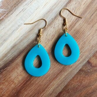 Teardrop earrings handmade in turquoise resin and hung from delicate gold tone ear wires. Displayed on a wooden backdrop.