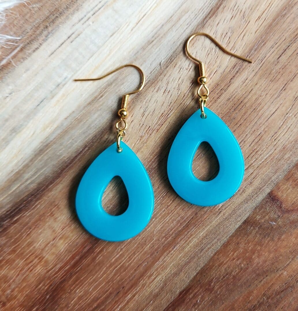 Teardrop earrings handmade in turquoise resin and hung from delicate gold tone ear wires. Displayed on a wooden backdrop.