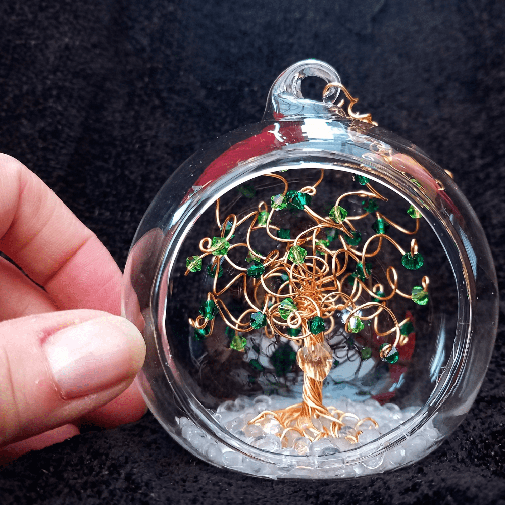 A miniature wire & crystal tree in an 8cm glass open fronted bauble with thumb & fingers next to it to give sizing.