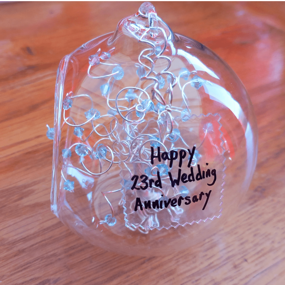 8cm glass bauble with a acrylic plaque that has a handwritten name in black ink. The clear acrylic is molded into the side of the bauble & wired onto it with silver wire.