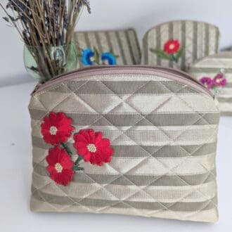 A gold quilted make up pouch with a red flower applique