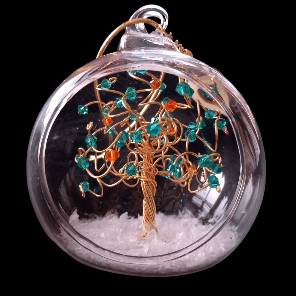 8cm glass bauble with an open front and a gold wire tree set into it on a glass pebble base. The tree has blue zircon and sun crystals on the branches and set into a snowy base.