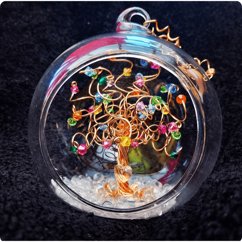 8cm glass bauble with an open front and a gold wire tree set into it on a glass pebble base. The tree has a multicoloured rainbow mix of crystals on the branches.