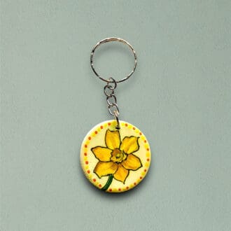 A handmade, hand painted wooden circular keyring with a daffodil design. Dots around the edge.