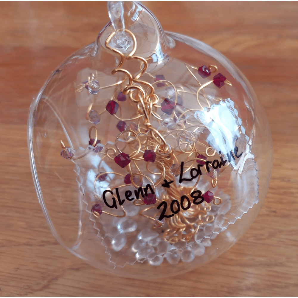 8cm glass bauble with a rectangular shape of clear acrylic that has been molded into the side of the bauble. It is handwritten on in black ink to capture a personalised message, and wired onto the bauble with gold wire.