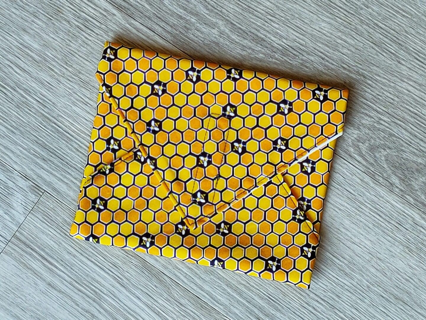 Reusable sandwich wrap with a honeycomb bee cotton outer fabric and food-safe PUL lining.