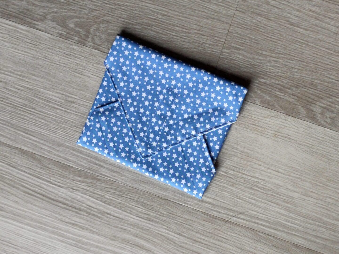 Reusable sandwich wrap with small white stars on light blue cotton outer fabric and food-safe PUL lining.