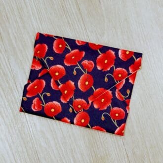 Reusable sandwich wrap with red poppies on a navy blue cotton outer fabric and food-safe PUL lining.