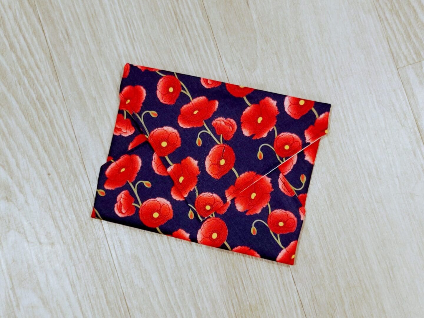 Reusable sandwich wrap with red poppies on a navy blue cotton outer fabric and food-safe PUL lining.