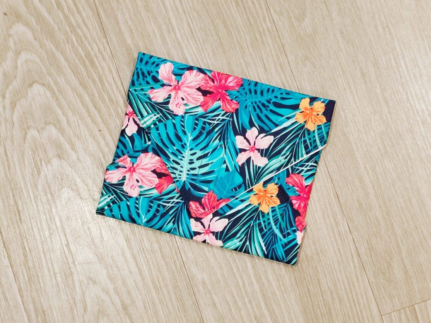 Reusable sandwich wrap with tropical flowers and leaves on a navy blue cotton outer fabric and food-safe PUL lining.