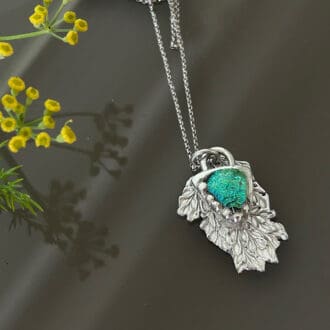 A fine silver 999 small leaf pendant with a blue and green fused glass cabochon sitting on the top.