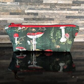 Pencil case or make up bag in dark green woodland fabric featuring fly algaric mushrooms and whimsical woodland folk, red zip and pale green lining.