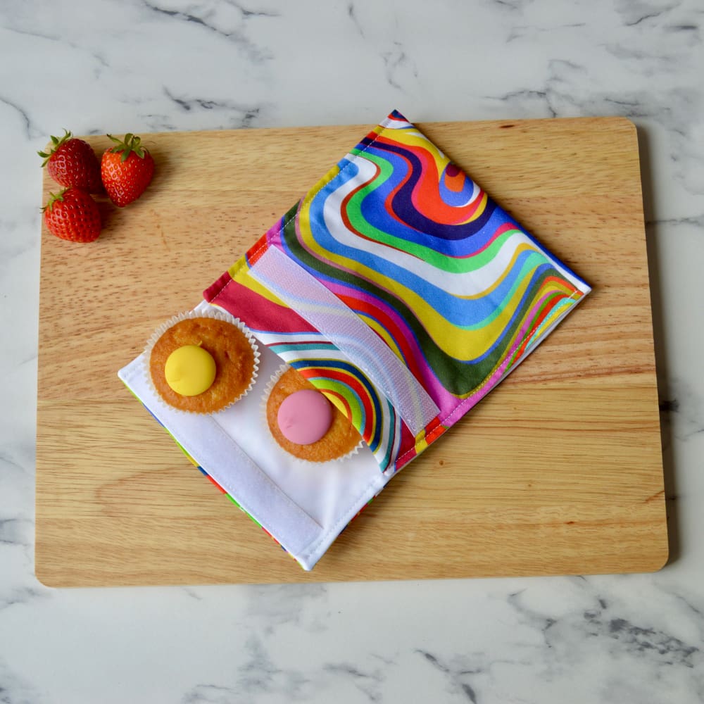 Retro rainbow multi coloured snack bag on a wooden board with cupcakes.