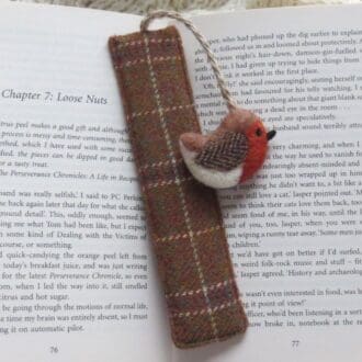 Bookmark made from brown checked wool fabric with a needle felted wool robin bird attached by a jute cord and placed on an open book.