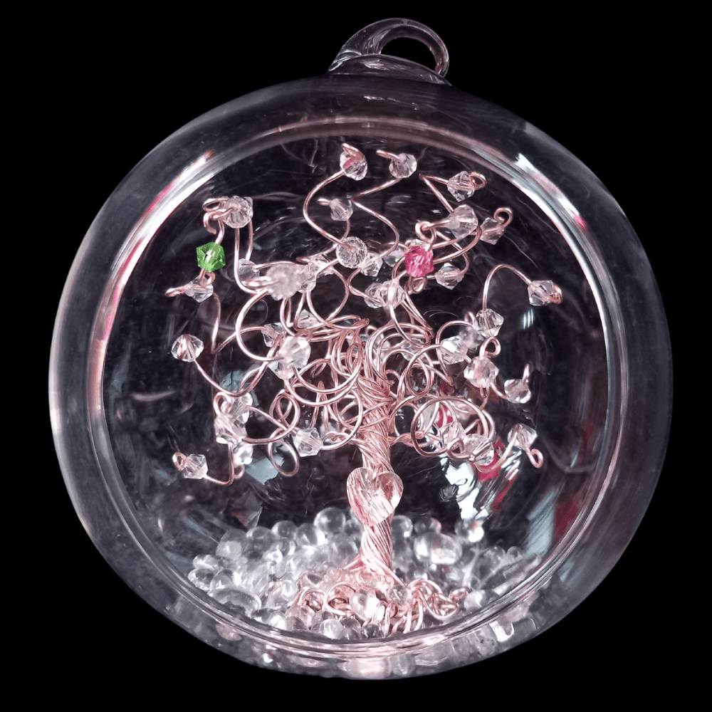 8cm glass open fronted bauble with a rose gold wire tree set inside, set on a glass pebble base. There is a clear crystal heart wired into the trunk of the tree. The branches are decorated with clear crystals and there are two birthstone drops - a peridot & rose crystal.