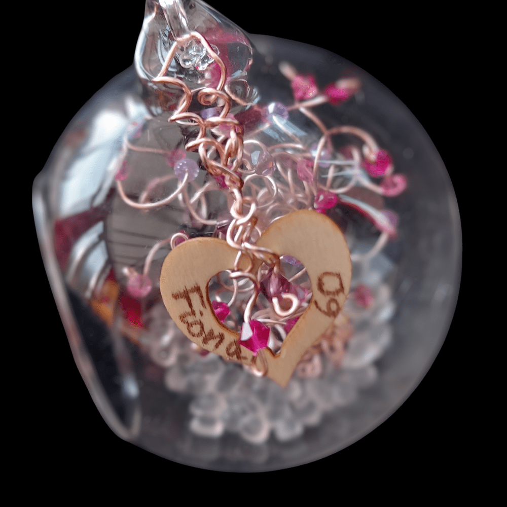 8cm glass bauble decorated with a wooden heart charm that is handwritten with a name and 60. The hear is decorated with two rose gold wire spirals with drup crystals in pink.