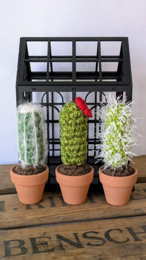 Set of Three Crochet Cacti in Front of a Black Decorative Greenhouse