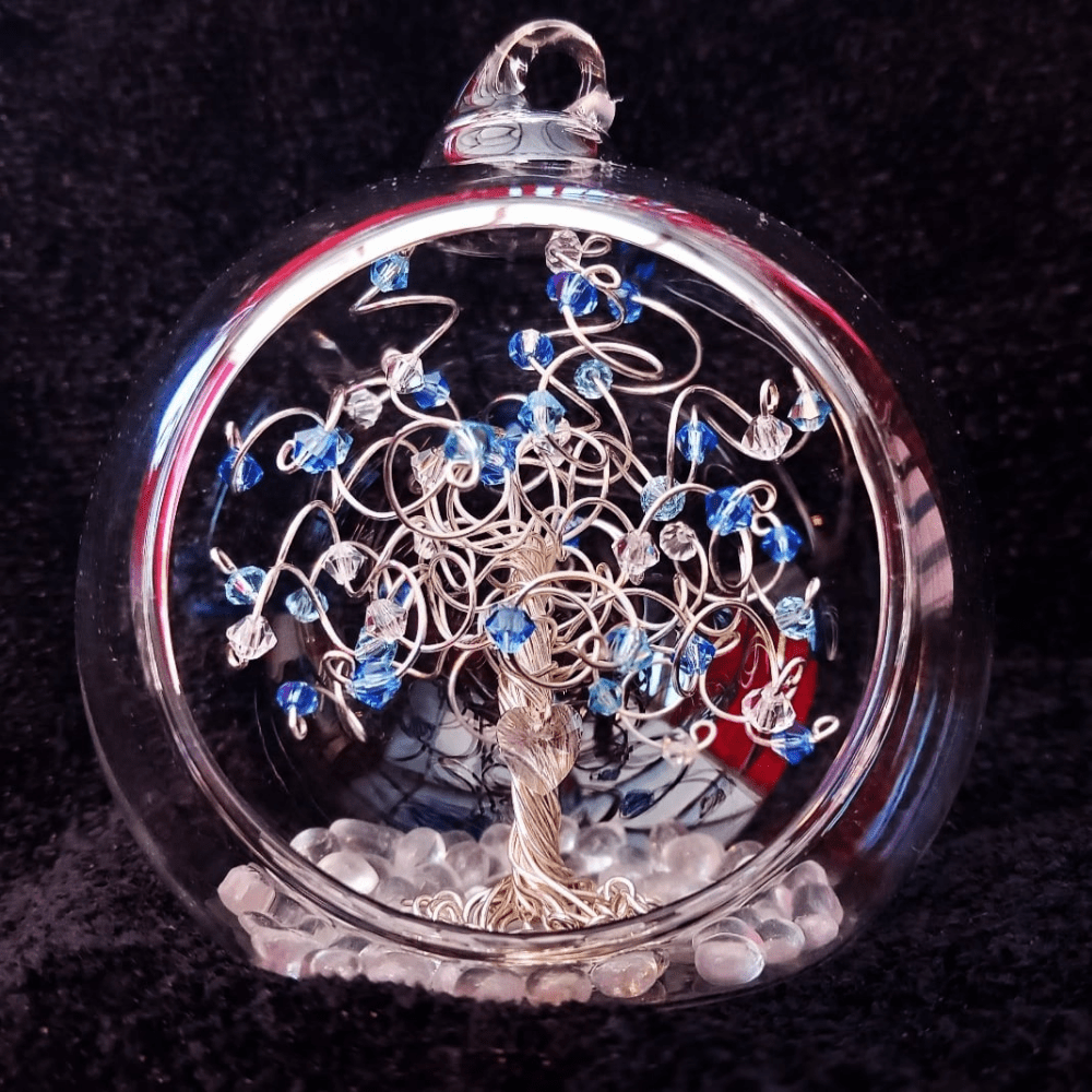 8cm glass open fronted bauble with a silver wire tree set inside on a glass pebble base. A clear glass heart is wired into the trunk, and the branches are decorated with a mix of sapphire, aquamarine & opal crystals.