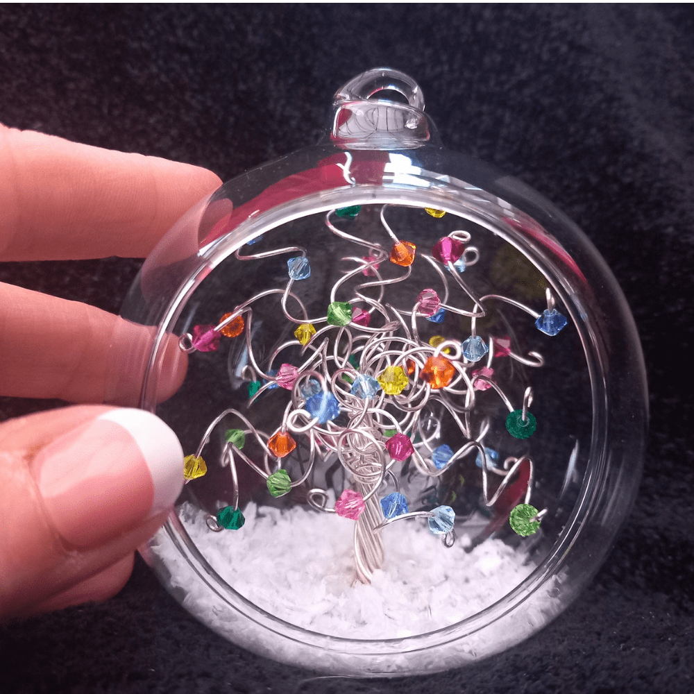 A miniature wire & crystal tree in an 8cm glass open fronted bauble with thumb & fingers next to it to give sizing.