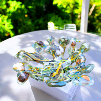 A colourful fused glass sculpture inspired by rockpools, featuring a vibrant mix of blue, green, yellow, and brown hues. The bowl has an irregular, organic shape with multiple protruding elements, capturing the essence of oceanic life.