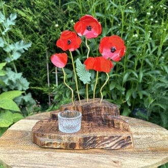 a stepped wooden base with 5 resin red poppies set in it on gold coloured wire with a glass round tealight holder