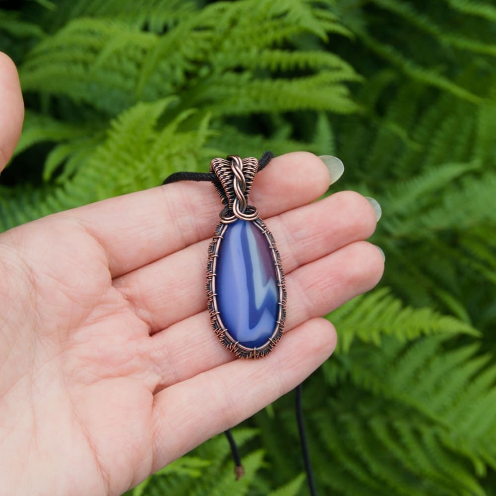 Hand holding a copper wire wrapped pendant with blue fused glass pebble