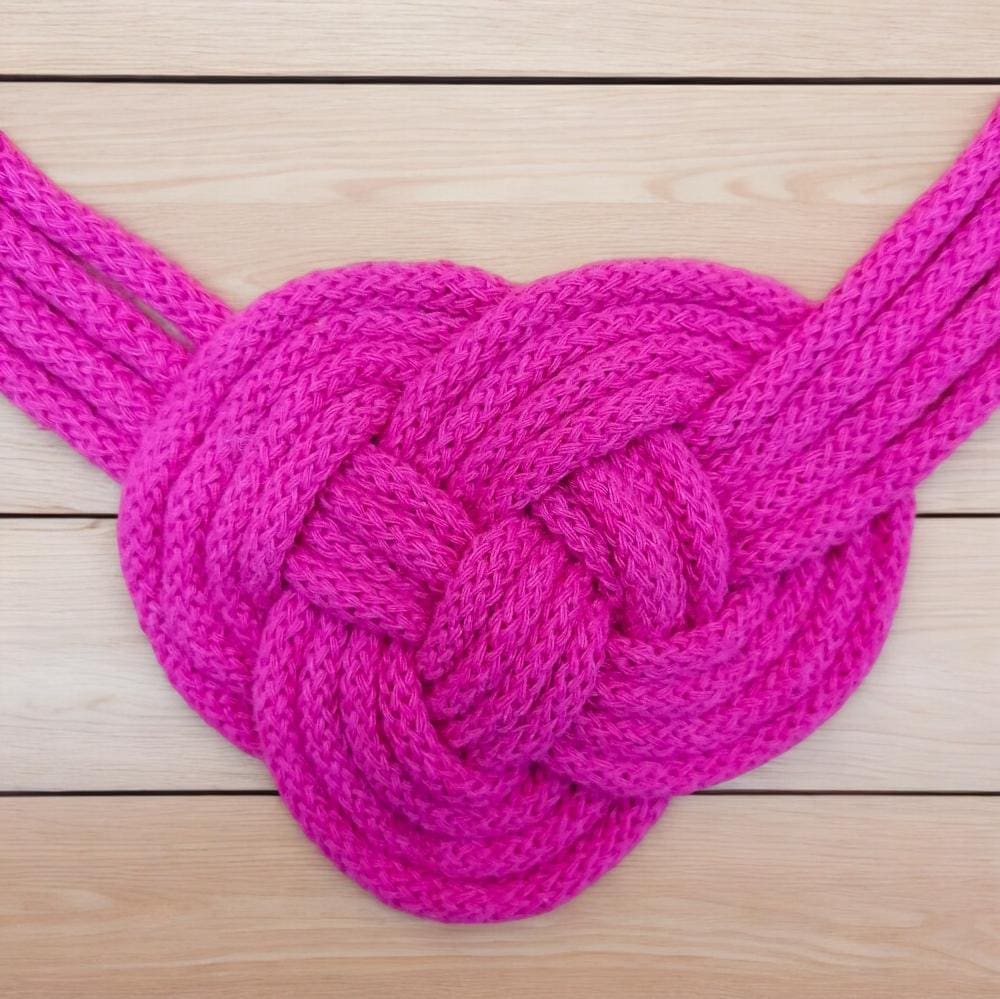 Pink statement necklace chunky knot feature close up against a pale wood floorboard background.