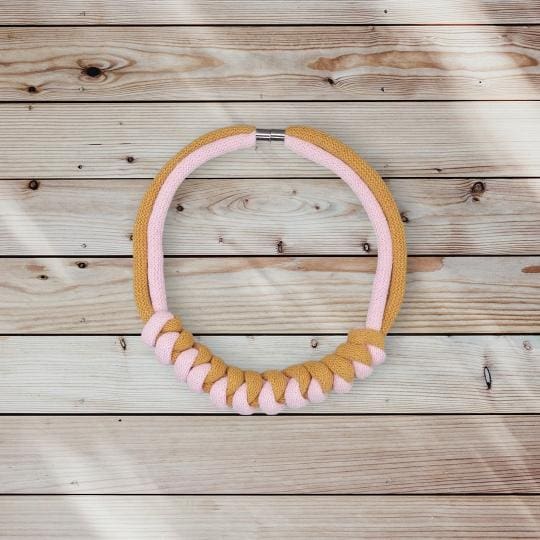 Overhead shot of pink and mustard chunky rope necklace against a light pine wooden background.