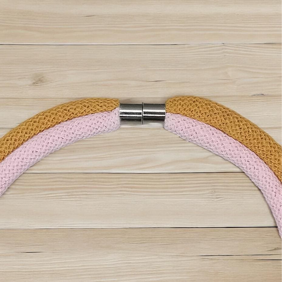 Magnetic clasp detail on chunky pink and mustard modern rope necklace shown against a light wooden background.