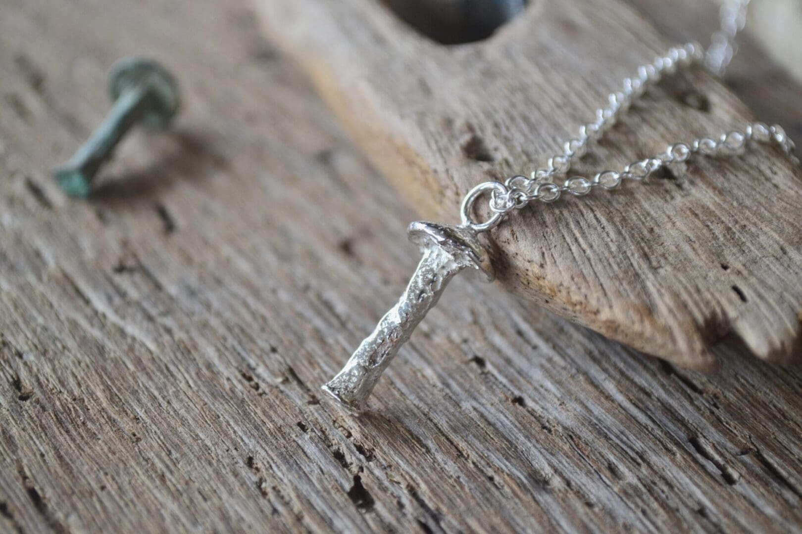 Solid silver mushroom pendant on a silver chain. in the background is the old rivet that the pendant was cast from.